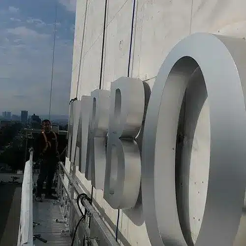 Sign installation for 'Harbor' high-rise signage with a technician working on a building facade during the day.