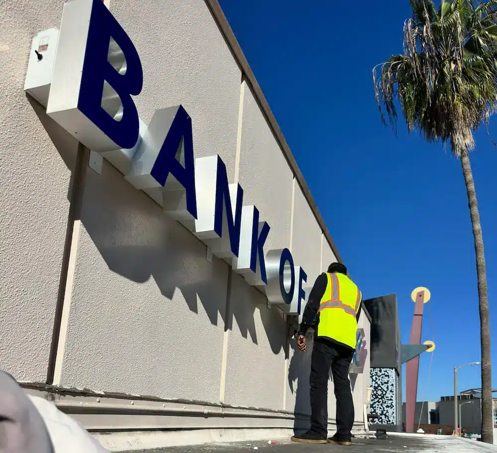 Sign installer mounting blue dimensional channel letters above a Burbank, CA storefront